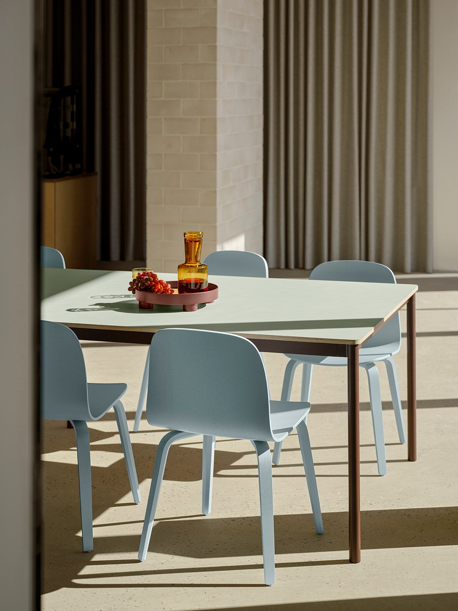 A base table in light green, brown, and red tones, paired wit  light blue Visu chairs placed in the sunlight.  A base table in light green, brown, and red tones, paired wit  light blue Visu chairs placed in the sunlight.